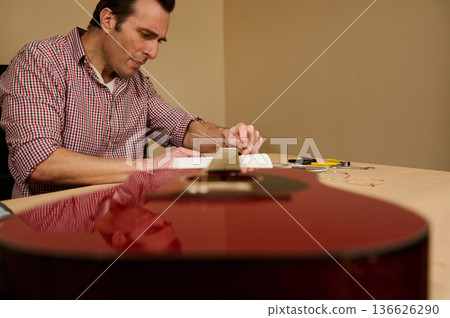 Man Changing Guitar Strings at a Table Focused on Maintenance and Repair Man Changing Guitar Strings at a Table Focused on Maintenance and Repair 136626290
