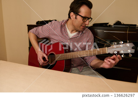 Man Adjusting Acoustic Guitar Strings at Home - Guitar Maintenance and Repair Practice Man Adjusting Acoustic Guitar Strings at Home - Guitar Maintenance and Repair Practice 136626297