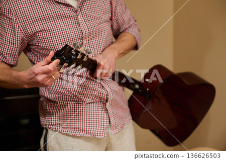 Man Adjusting Guitar Strings While Holding Acoustic Guitar - Guitar Maintenance and Repair Man Adjusting Guitar Strings While Holding Acoustic Guitar - Guitar Maintenance and Repair 136626503