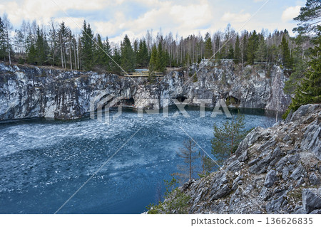 Icy lake in Ruskeala mountain park surrounded by marble quarry cliffs and evergreen forest. Northern nature travel and winter landscape. Icy lake in Ruskeala mountain park surrounded by marble quarry cliffs and evergreen forest. Northern nature travel and winter landscape. 136626835