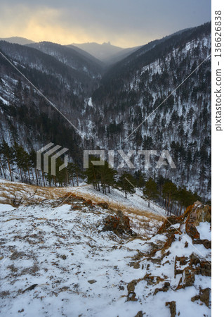 Valley in snowy mountains with forest trees and orange sky. Winter landscape for travel and nature concept. Scenic view of wild landscape. Krasnoyarsk Stolby park. Valley in snowy mountains with forest trees and orange sky. Winter landscape for travel and nature concept. Scenic view of wild landscape. Krasnoyarsk Stolby park. 136626838