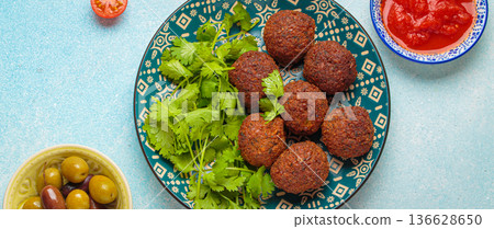 Falafel with tomato sauce, green olives and coriander leaves on blue background top view Falafel with tomato sauce, green olives and coriander leaves on blue background top view 136628650