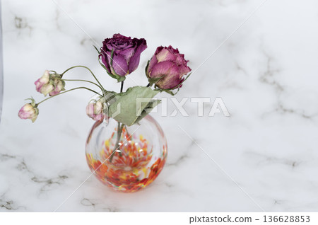 Dried purple roses and small flowers in a warm-colored glass vase (left) 136628853