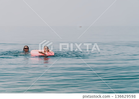 Mother daughter swimming mother and young daughter enjoying a sunny day at the sea with a pink inflatable ring Mother daughter swimming mother and young daughter enjoying a sunny day at the sea with a pink inflatable ring 136629598