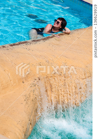 A woman swims in a pool with a waterfall A woman swims in a pool with a waterfall 136629919