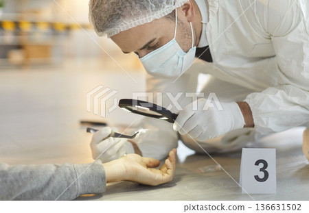 Forensic expert examining corpse hand with magnifying glass collecting evidence at the crime scene. Forensic expert examining corpse hand with magnifying glass collecting evidence at the crime scene. 136631502