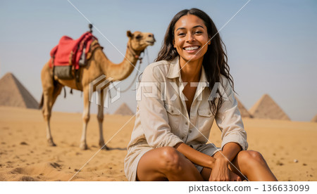 A young woman sits and poses for the camera against the backdrop of the Great Pyramids and the sky. 136633099