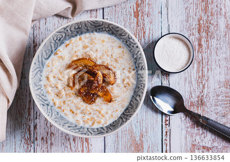 Oatmeal with caramelized apples and coconut flakes in a bowl on the table top view Oatmeal with caramelized apples and coconut flakes in a bowl on the table top view 136633854