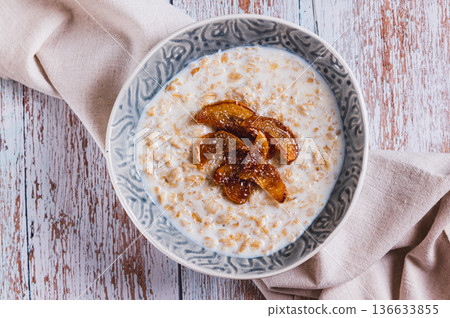 Close up of oatmeal with caramelized apples and coconut flakes in a bowl top view Close up of oatmeal with caramelized apples and coconut flakes in a bowl top view 136633855
