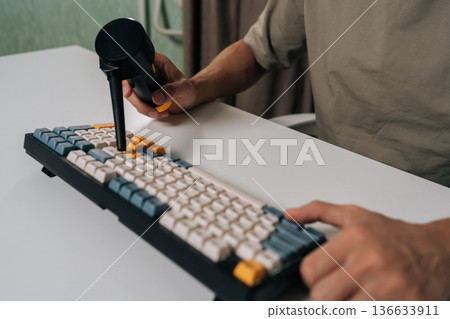 Person using electric air duster for cleaning mechanical wireless keyboard, performing maintenance and ensuring hygiene for optimal computing performance and technology care, close-up. 136633911