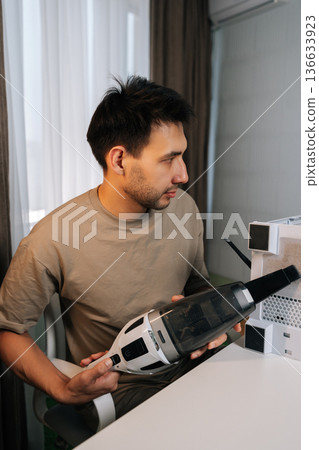Vertical shot of man cleaning computer system unit with vacuum cleaner, removing dust from dirty air filter and mesh panel, providing essential pc maintenance, hardware care for optimal performance. 136633923