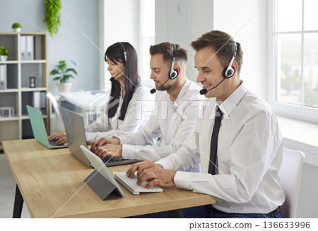 Support agents with headsets working on laptops in a bright modern office Support agents with headsets working on laptops in a bright modern office 136633996