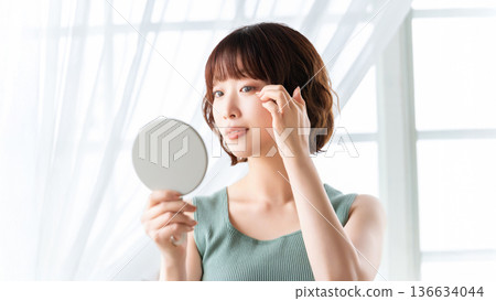 Woman checking her eyes in the mirror, beauty image 136634044