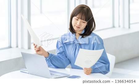 A woman/businesswoman looking at documents and thinking 136634054