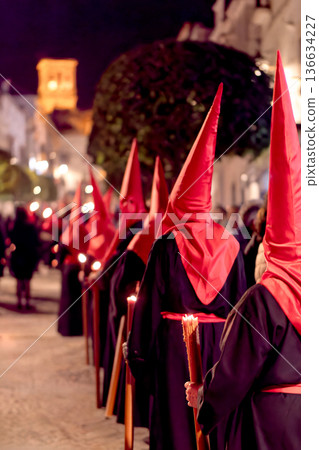 Many nazarenos with red hoods walking in procession Many nazarenos with red hoods walking in procession 136634227