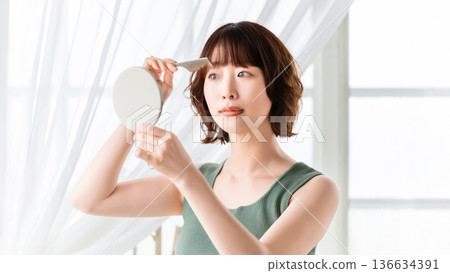 Woman looking in the mirror and arranging her hair, beauty image 136634391