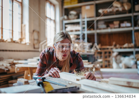 Female carpenter working on her product in carpentry workshop. Female carpenter working on her product in carpentry workshop. 136634834