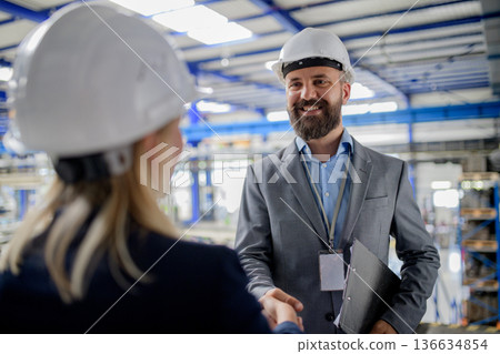Business partners shaking hands during factory meeting. 136634854
