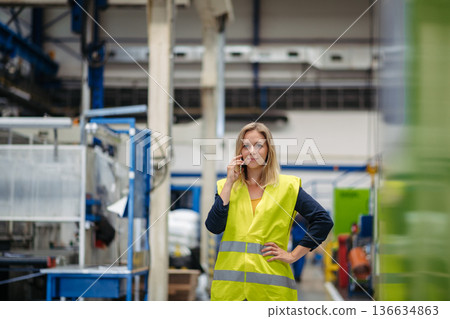 Female factory supervisor talking on phone in industrial production hall. Female factory supervisor talking on phone in industrial production hall. 136634863