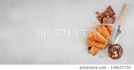 Croissant with chocolate spread hazelnuts and knife top view banner 136635730