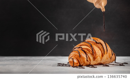 Chocolate drizzle over croissant on dark background with copy space 136635740