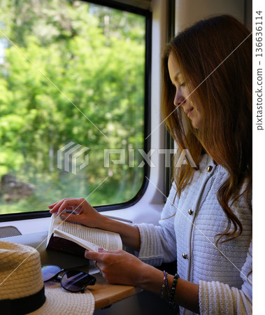 Woman reading book by train window in summer countryside 136636114