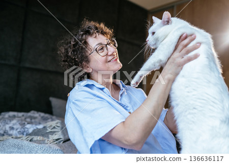 joyful playful mood, glasses, smiling woman holding large white cat, pet bonding, home bedroom, soft morning light, cozy weekend moment, White, forties, animal care, affectionate interaction joyful playful mood, glasses, smiling woman holding large white cat, pet bonding, home bedroom, soft morning light, cozy weekend moment, White, forties, animal care, affectionate interaction 136636117