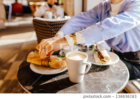Close-up of woman hands reaching for fresh sandwich on marble cafe table with coffee cup. Real life breakfast moment, urban coffee culture, slow living, casual lifestyle, authentic everyday food Close-up of woman hands reaching for fresh sandwich on marble cafe table with coffee cup. Real life breakfast moment, urban coffee culture, slow living, casual lifestyle, authentic everyday food 136636163