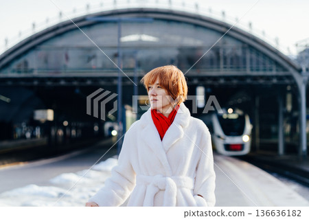 Caucasian redhead adult woman standing on railway platform, white coat and red scarf, thoughtful attentive expression, modern train in background, winter city rail travel pause Caucasian redhead adult woman standing on railway platform, white coat and red scarf, thoughtful attentive expression, modern train in background, winter city rail travel pause 136636182