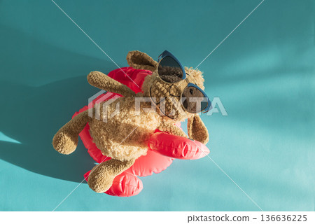 Knitted Plush Sheep in Sunglasses on Pink Flamingo Float Against Blue Water. Top view Knitted Plush Sheep in Sunglasses on Pink Flamingo Float Against Blue Water. Top view 136636225