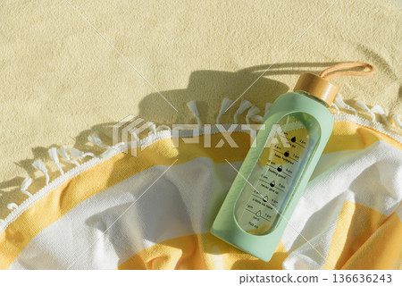 Green Water Bottle with Motivational Time Markers on Beach Towel. Summer Hydration Concept Green Water Bottle with Motivational Time Markers on Beach Towel. Summer Hydration Concept 136636243