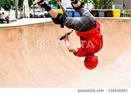 Young man practicing Scootering (Freestyle Scootering) in the new SkatePark in the central park of Igualada, Barcelona, Spain. 136636901