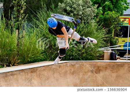 Young man practicing Scootering (Freestyle Scootering) in the new SkatePark in the central park of Igualada, Barcelona, Spain. Young man practicing Scootering (Freestyle Scootering) in the new SkatePark in the central park of Igualada, Barcelona, Spain. 136636904