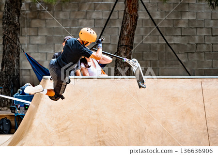 Young man practicing Scootering (Freestyle Scootering) in the new SkatePark in the central park of Igualada, Barcelona, Spain. 136636906