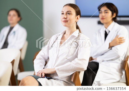 Diligent woman medical student with group of other interns listening lecture at lesson in university Diligent woman medical student with group of other interns listening lecture at lesson in university 136637354