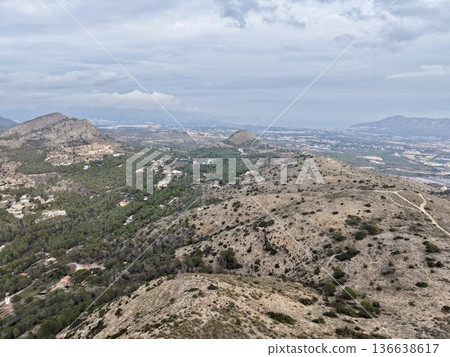 Trail Runner Navigating Rugged Ridge With Sparse Vegetation And Distant Cityscape On Horizon Trail Runner Navigating Rugged Ridge With Sparse Vegetation And Distant Cityscape On Horizon 136638617