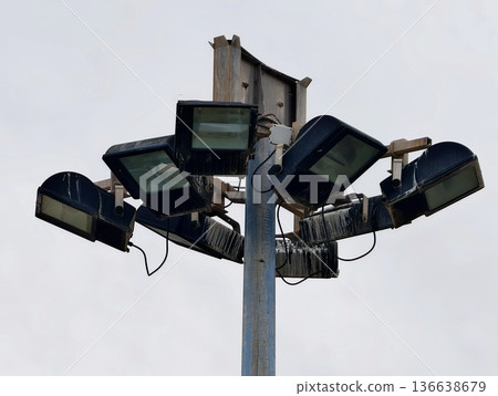 Cluster Of Lighting Fixtures On Pole Under Cloudy Skies Displaying Worn Paint And Rugged Materials 136638679