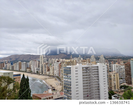 Cityscape With Beach And Mountains, City Along Coast With Misty Mountains And Reflective Wet Sands 136638741