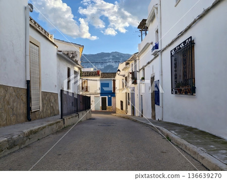 Luminous Midday Scene Showcasing Petite Street Lined With White Structures And Scenic Coastal Mountain View 136639270