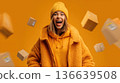 Excited woman in yellow winter coat and beanie surrounded by floating packages against a vibrant orange background 136639508