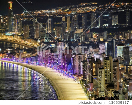 Bright Coastal Night Scene, Vivid Nighttime Image Of Illuminated Shoreline And Lively Beach Party 136639517