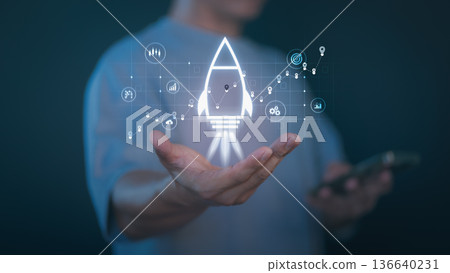 Person holding a glowing rocket icon with digital analytics, graph, and startup symbols representing business growth, innovation, startup launch, success strategy, and digital marketing development. Person holding a glowing rocket icon with digital analytics, graph, and startup symbols representing business growth, innovation, startup launch, success strategy, and digital marketing development. 136640231