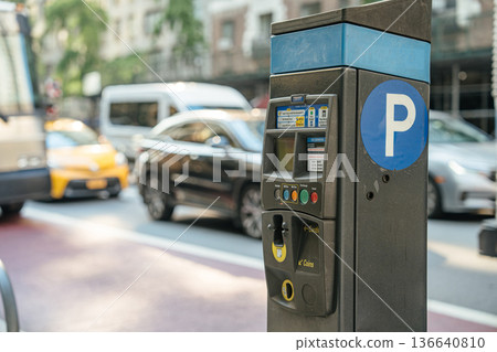 A close-up of a parking meter with a large "P" sign on a Manhattan street. Blurred traffic, including taxis and cars, moves in the background. 136640810