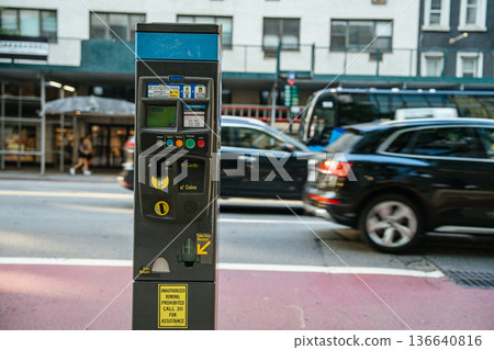 A modern parking meter stands on a busy New York City street with cars passing in the background. The machine accepts cards and coins for payment. A modern parking meter stands on a busy New York City street with cars passing in the background. The machine accepts cards and coins for payment. 136640816