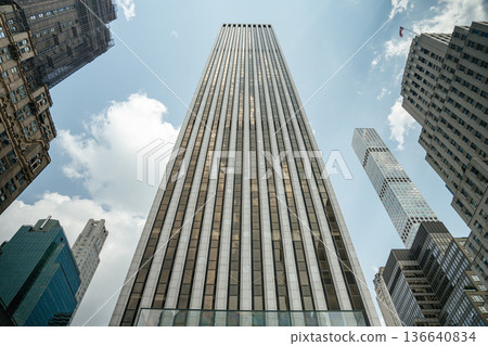 A towering modern skyscraper rises dramatically into the sky, surrounded by other iconic buildings in Midtown Manhattan. The low-angle view highlights the vertical lines and architectural contrast 136640834