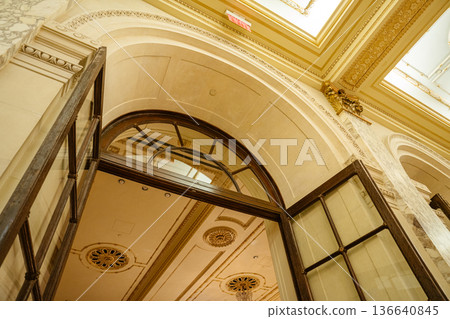 A classic arched doorway with wooden-framed glass doors opens into an ornate interior with decorative ceiling details. Marble columns, intricate molding, and warm lighting enhance the timeless 136640845