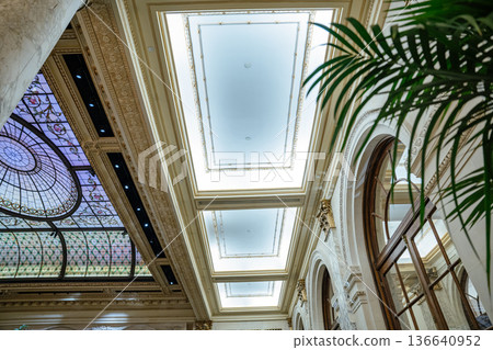 Elegant view of a historic hotel ceiling featuring stained glass panels, ornate molding, and arched windows. The architectural design combines luxury elements with classical artistry and natural light 136640952