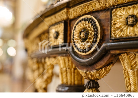 A macro shot captures the intricate gold and black carved ornamentation of a luxurious antique table. The blurred background enhances the craftsmanship and elegance of the design. A macro shot captures the intricate gold and black carved ornamentation of a luxurious antique table. The blurred background enhances the craftsmanship and elegance of the design. 136640963