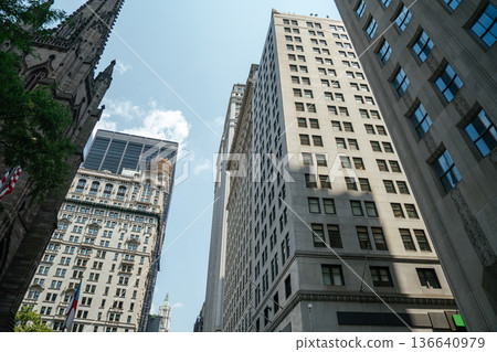 Skyscrapers rise alongside a historic church in Manhattan's Financial District. The image captures the contrast between modern business towers and old architecture. 136640979