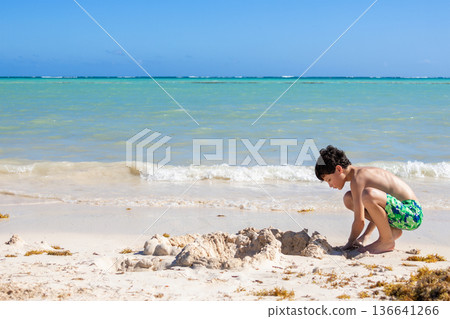 Teen boy is playing with white sand at the tropical beach. Teen boy is playing with white sand at the tropical beach. 136641266